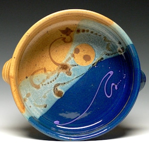 May include: A ceramic bowl with a blue and brown glaze. The bowl has a unique design with a swirl of blue and brown glaze. The bowl is perfect for serving soup, salad, or other dishes.