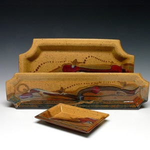 May include: Set of three ceramic serving trays in various shades of brown, red, and gold with a speckled glaze. The trays are rectangular with rounded corners and feature a decorative design.