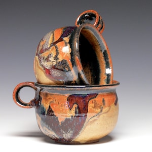 May include: Two ceramic mugs with a brown, orange, and black glaze. The mugs have a unique, hand-crafted look.