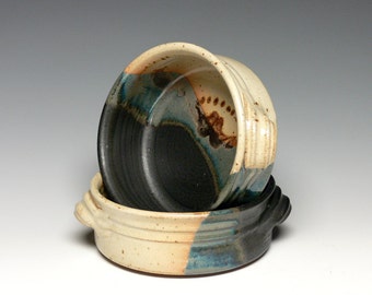 May include: Two ceramic bowls with a white, blue, and black glaze. The bowls have a rounded shape and a lip around the top. The bowls are stacked on top of each other.