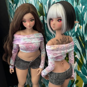 Könnte beinhalten: Zwei Puppen tragen passende schulterfreie Langarm-Bauchfrei-Tops mit einem pastellfarbenen rosa, blauen und weißen Wolken- und Sternenmuster, kombiniert mit dunkelgrauen Jeansshorts. Eine Puppe hat langes braunes Haar, die andere kurzes schwarz-weißes Haar.