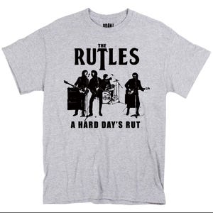 May include: A light gray t-shirt featuring a black and white graphic of a band performing. The band name "THE RUTLES" is printed above the band illustration, with the phrase "A HARD DAY'S RUT" below.