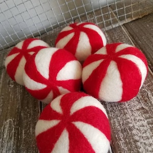 K&ouml;nnte beinhalten: Sechs rote und wei&szlig;e Wollkugeln in Pfefferminzform. Die Kugeln sind in einem Halbkreis auf einer Holzoberfl&auml;che angeordnet.