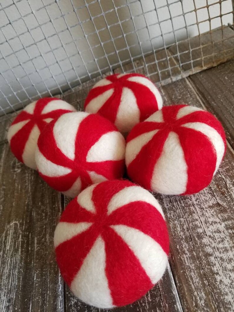 K&ouml;nnte beinhalten: Sechs rote und wei&szlig;e Wollkugeln in Pfefferminzform. Die Kugeln sind in einem Halbkreis auf einer Holzoberfl&auml;che angeordnet.
