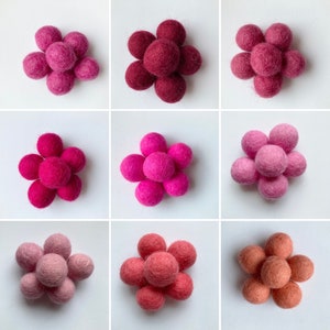 May include: Nine felt balls arranged in a flower shape. The balls are in three different shades of pink, from light to dark.