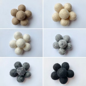 May include: Six felt balls arranged in a flower shape. The balls are in four different colors: beige, white, gray, and black.