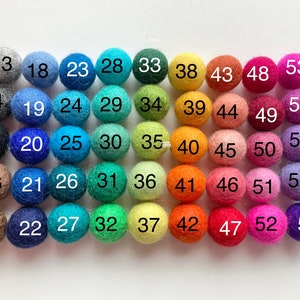May include: A color chart of 57 felt balls, arranged in rows of 9, with numbers 13 through 57 printed on each ball. The balls are in a variety of colors, including gray, blue, green, yellow, orange, red, pink, purple, and brown.