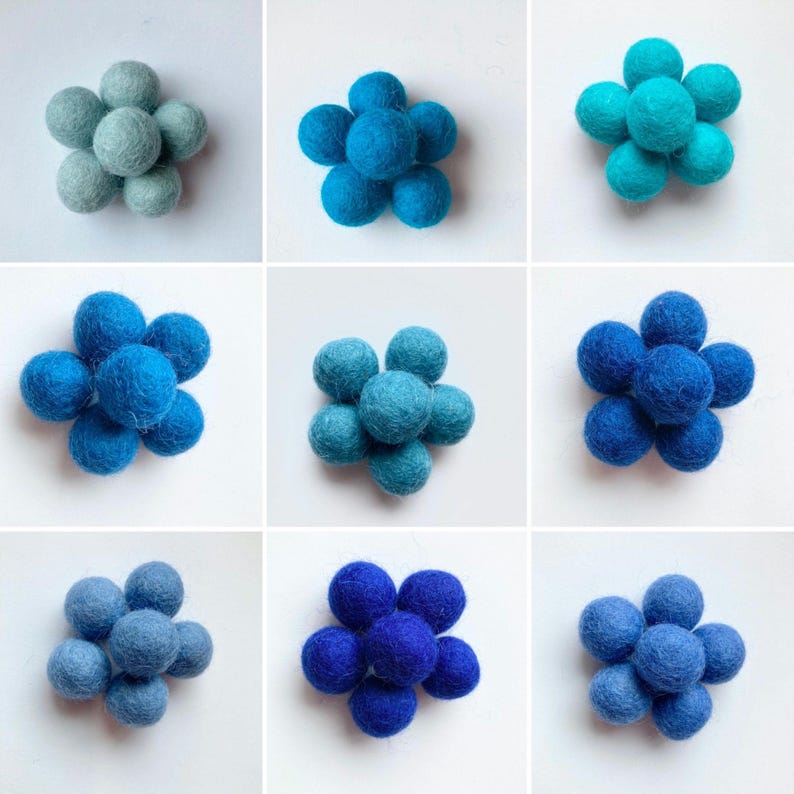 May include: Nine felt balls arranged in a flower shape. The balls are in shades of blue, from light blue to dark blue.