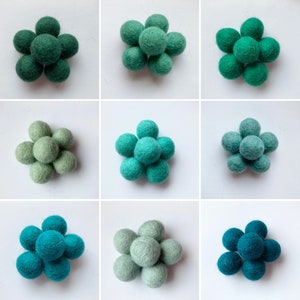 May include: Nine felt balls arranged in a flower shape. The balls are in shades of green, from light to dark.