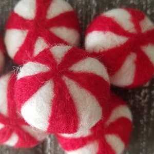 May include: A group of six red and white felt peppermint candies. The candies are round and have a swirl pattern.