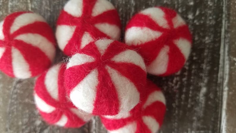 May include: A group of six red and white felt peppermint candies. The candies are round and have a swirl pattern.