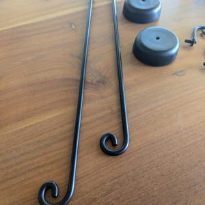 May include: Black metal decorative hardware components, including two long rods with curled ends, two round black bases, and other small parts. The components are arranged on a wooden surface.