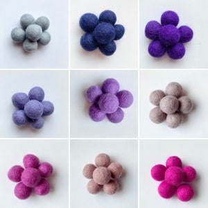 May include: Nine felt balls arranged in a flower shape. The balls are in three different colors: gray, purple, and blue.