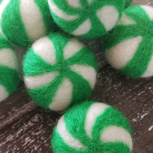 May include: A group of six green and white felt balls with a peppermint swirl design. The balls are soft and fuzzy and would be great for a craft project or a child's toy.