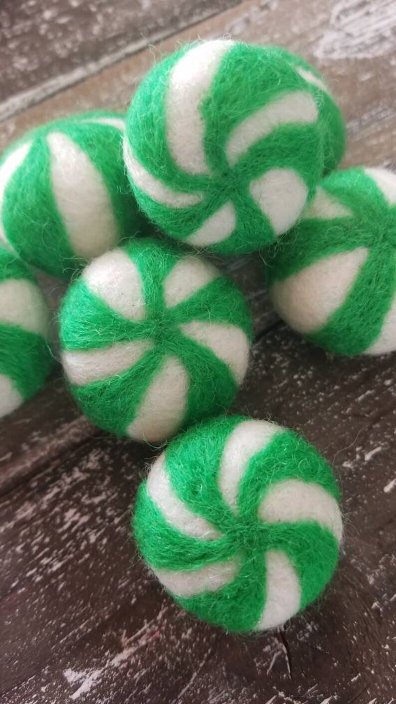 May include: A group of six green and white felt balls with a peppermint swirl design. The balls are soft and fuzzy and would be great for a craft project or a child's toy.