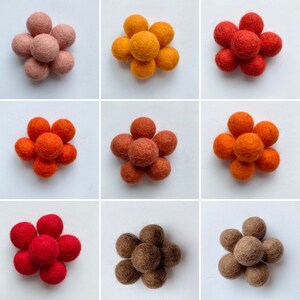 May include: Nine felt balls arranged in a flower shape. The balls are in shades of orange, red, brown, and pink.