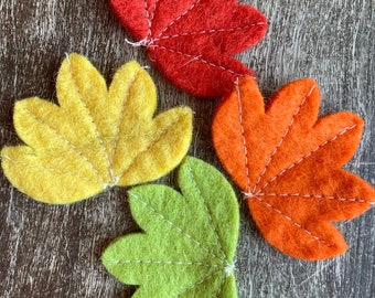 May include: Four felt leaves in different colors: red, yellow, orange, and green. Each leaf has a stitched design and is shaped like a five-pointed star.
