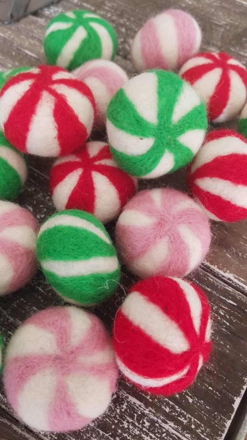 May include: A collection of felt ornaments shaped like peppermint candies. The ornaments are in red, green, pink, and white.