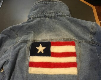 May include: A blue denim jacket with a felt American flag patch on the back. The flag is red, white, and blue with a white star in the blue canton.