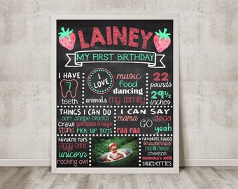 May include: A chalkboard style first birthday sign with a pink and green color scheme. The sign features a photo of a baby girl, along with details about her first year, including her weight, height, favorite foods, and things she can do. The sign is decorated with strawberries and the text "LAINEY MY FIRST BIRTHDAY".