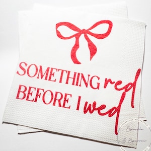 May include: White paper napkins with red text and a red bow design. The text reads "SOMETHING red BEFORE I wed". The napkins are stacked and suitable for a wedding or bridal shower.