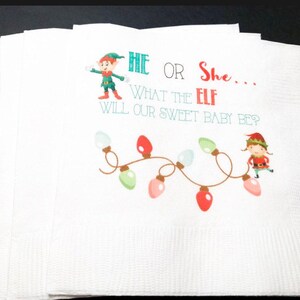 May include: White paper napkins with a festive design. The napkins feature the text "He or She... What the Elf Will Our Sweet Baby Be?" along with illustrations of elves and colorful Christmas lights.