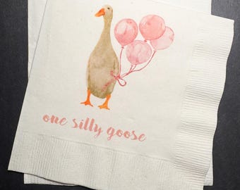 May include: White paper napkins with a watercolor illustration of a goose holding pink balloons. The text "one silly goose" is printed in pink below the goose. The napkins are stacked on a dark surface.