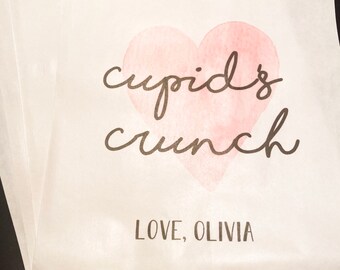 May include: White paper bags with a pink watercolor heart and the text "cupid's crunch" and "LOVE, OLIVIA".