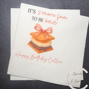 May include: White paper napkins with a watercolor illustration of a s'more, a graham cracker sandwich with marshmallow and chocolate, topped with a pink bow. Text reads "IT'S s'more fun TO BE one" and "Happy Birthday Callie!"