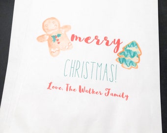May include: White paper gift bag with a gingerbread man and a Christmas tree design. The text reads "merry christmas! Love, The Walker Family."