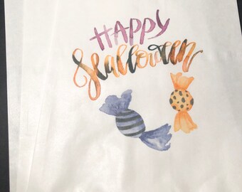 May include: White paper gift bag with a watercolor design of two candy pieces and the text "Happy Halloween".