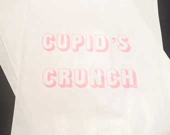 May include: White paper bag with pink text that reads "CUPID'S CRUNCH".