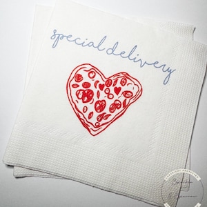 May include: White paper napkins with a red heart-shaped pizza design and the words "special delivery" in light blue script. The pizza has red toppings. The napkins are stacked.