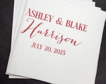 May include: White paper napkins with a textured surface, stacked on top of each other. The napkins have the names "Ashley & Blake Harrison" and the date "July 20, 2025" printed in red script.