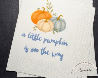 May include: White paper napkins with a watercolor illustration of three pumpkins in orange, cream, and blue-green, with green leaves. The text "a little pumpkin is on the way" is written in blue script.
