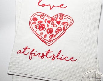 May include: White paper napkins with a red heart-shaped pizza design and the words "love at first slice." The pizza has red toppings. The napkins are stacked.