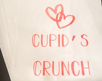 May include: White paper bag with a red heart design and the text "CUPID'S CRUNCH" printed on it.