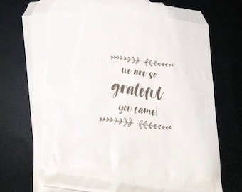 May include: White paper bags with a black printed message that reads "We are so grateful you came!" with a simple floral design above and below the text.