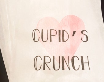 May include: White paper bags with a pink watercolor heart and the text "CUPID'S CRUNCH" printed on them.
