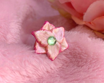 May include: A pink and white flower with a green gem in the centre. The flower is made of polymer clay and is a handmade piece of jewellery.