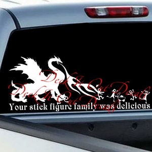 Peut inclure: Autocollant en vinyle blanc représentant un dragon poursuivant des personnages en bâton, avec le texte "Deck It Out, Your stick figure family was delicious" en rouge et blanc. Appliqué sur la vitre arrière d'un pick-up argenté.