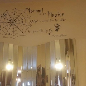 May include: A white wall with a black spider web and a quote that reads "Normal is an illusion. What is normal for the spider is chaos for the fly. - Morticis Ades"