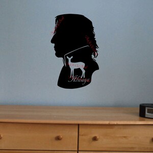 Könnte beinhalten: Eine schwarze Silhouette eines Männerkopfes mit einer weißen Hirsch-Silhouette im Inneren. Der Text "Always" befindet sich unterhalb des Hirsches. Die Silhouette befindet sich an einer hellblauen Wand über einer Kommode aus Holz.