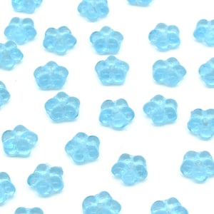 May include: A scattering of light blue glass flower beads. The beads are small and have a five-petal flower shape.