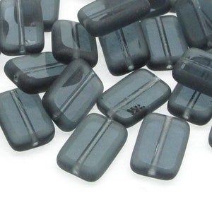 May include: A pile of dark gray glass beads with a rectangular shape and a subtle line down the center of each bead.