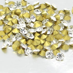May include: A pile of gold and clear rhinestones, scattered on a white surface.
