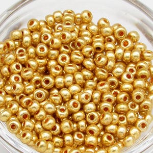 May include: A bowl filled with gold seed beads. The beads are small and round, and they have a metallic sheen.