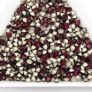 May include: A pile of red and silver rhinestones in a triangular shape. The rhinestones are small and have a pointed back.