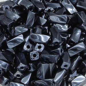 May include: A bowl filled with black faceted glass beads. The beads are shaped like small, elongated pyramids with a hole at the top.