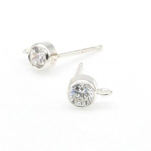 May include: A pair of silver earring posts with clear round cubic zirconia stones and a small loop on the back.